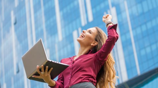 Businesswoman is the winner of agreement between companies in the city. Woman with long hair is the professional. She is holding laptop and big laughing.