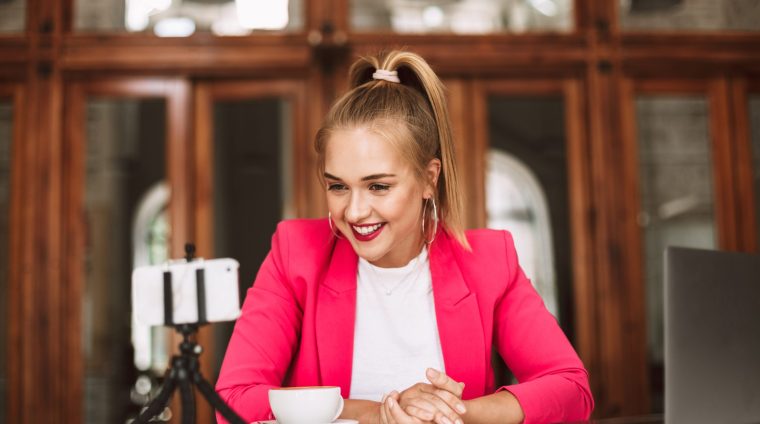 Young cheerful blogger in pink jacket happily recording new video for vlog