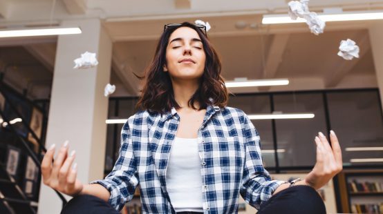 Relaxing time joyful young brunette woman having meditation on table in office surround flying papers. Taking a break, pause, smart student, relaxation, great success, dreaming