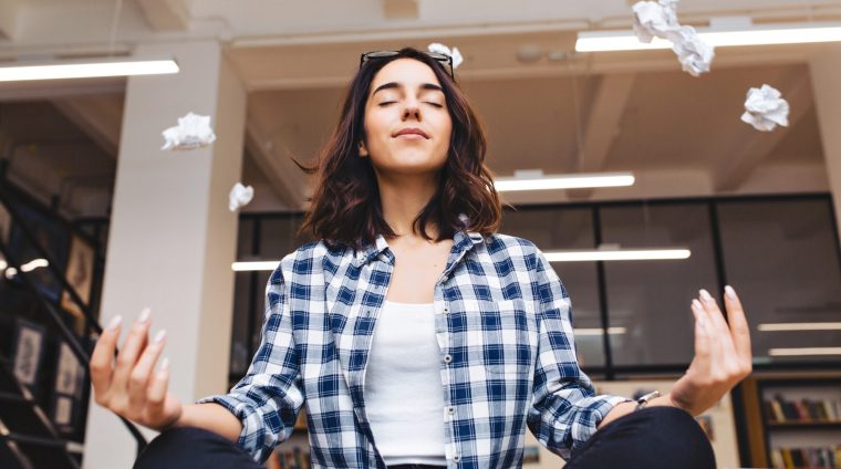 Relaxing time joyful young brunette woman having meditation on table in office surround flying papers. Taking a break, pause, smart student, relaxation, great success, dreaming